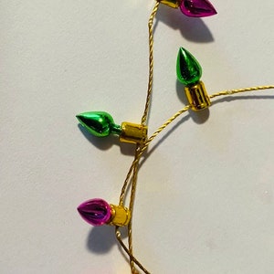May include: A string of miniature Christmas lights with green, pink, and red bulbs. The lights are strung on a gold wire.