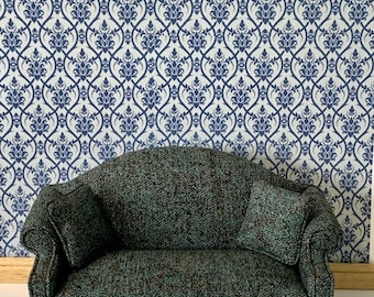 May include: A teal green tufted sofa with a curved back and wooden legs. The sofa has two pillows and is in front of a white and blue patterned wallpaper.