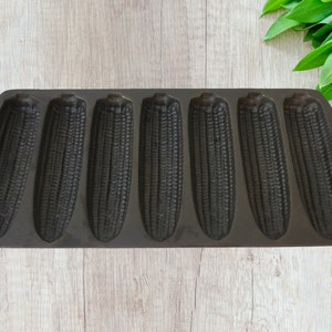May include: A black cast iron corn on the cob baking pan with eight individual molds. The pan is designed to hold corn on the cob for baking or grilling.