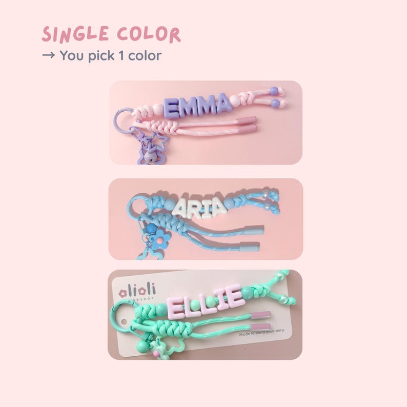 Peut inclure: Trois porte-cl&eacute;s personnalis&eacute;s avec les noms "EMMA", "ARIA" et "ELLIE". Chaque porte-cl&eacute;s pr&eacute;sente une combinaison de couleurs diff&eacute;rente, notamment rose, bleu et vert. Le texte "SINGLE COLOR" et "You pick 1 color" est en haut.