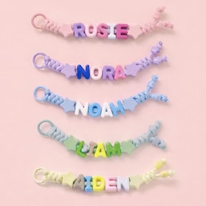 Peut inclure: Cinq porte-clés en cordon tressé avec des perles lettres en plastique formant les prénoms ROSIE, NORA, NOAH, LIAM et AIDEN. Chaque porte-clé comporte des perles en forme d'étoile aux extrémités de la séquence de lettres et un anneau.