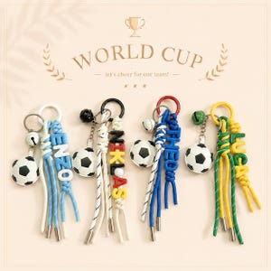 May include: A collection of keyrings with football charms and personalised names. Each keyring has a small football, a bell, and a name in colourful letters. The background includes the text "WORLD CUP".