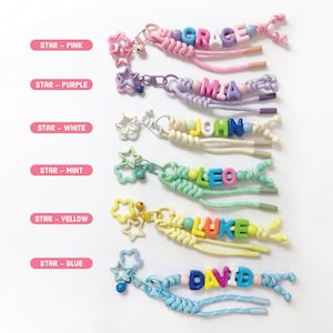 Peut inclure: Une collection de porte-cl&eacute;s personnalis&eacute;s avec des noms &eacute;pel&eacute;s en perles de lettres color&eacute;es. Chaque porte-cl&eacute;s comprend un charm en forme d'&eacute;toile et un cordon tress&eacute; de diff&eacute;rentes couleurs, dont rose, violet, blanc, menthe, jaune et bleu. Les noms incluent GRACE, MIA, JOHN, LEO, LUKE et DAVID.