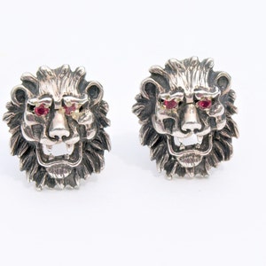 May include: A pair of silver lion head cufflinks with red gemstone eyes.