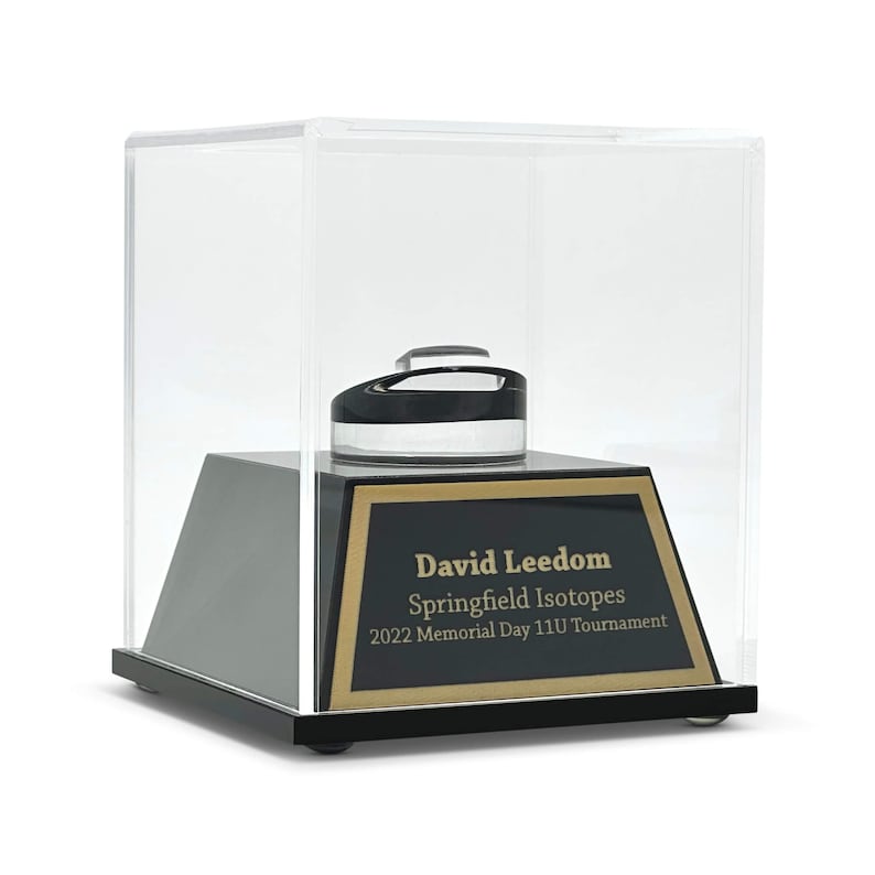 May include: A black and clear display case with a black base and a gold-trimmed plaque. The plaque reads "David Leedom Springfield Isotopes 2022 Memorial Day 11U Tournament". Inside the case is a black and clear object.