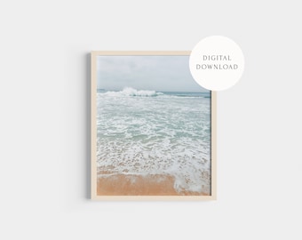 May include: A framed wall art print featuring a photograph of a sandy beach with light brown sand and turquoise ocean waves crashing toward the shore under a cloudy sky. A white circular badge in the top right corner reads DIGITAL DOWNLOAD.