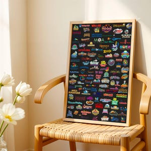 May include: A framed poster featuring numerous amusement park logos on a black background. The logos are in various colors and styles, with names like "Walibi," "Disney Resort," and "Hershey Park." The poster is displayed on a wooden chair.