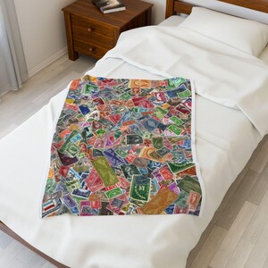 May include: A blanket featuring a vibrant collage of postage stamps in various colours. The stamps are of different sizes and shapes, with a mix of red, green, blue, and yellow. The blanket is on a white bed.