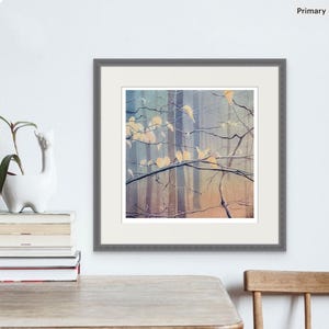 May include: A framed watercolor print of a forest scene. The artwork features a muted color palette with vertical tree trunks and branches with yellow leaves. The frame is gray, and the artwork is displayed on a white wall.