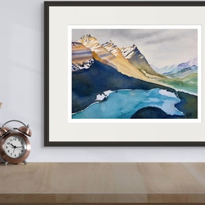 Pode incluir: Uma pintura a aquarela emoldurada que retrata uma cordilheira com um lago em primeiro plano. As montanhas s&atilde;o uma mistura de marrom, amarelo e branco, com neve nos picos. O lago &eacute; de um azul vibrante, com algumas pequenas ilhas. O c&eacute;u &eacute; cinza claro, com algumas nuvens.