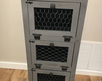 May include: A gray wooden cabinet with three drawers. Each drawer has a wire mesh front and a metal handle. The cabinet has a distressed finish.