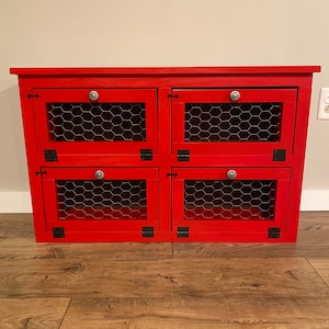 May include: Red wooden cabinet with four doors, each with a wire mesh insert and a silver knob. The cabinet has black hinges and sits on a wood floor.