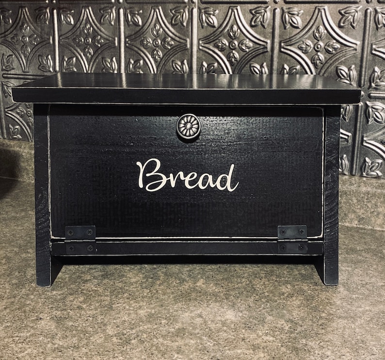K&ouml;nnte beinhalten: Schwarze Brotbox aus Holz mit einer wei&szlig;en Aufschrift "Brot". Die Box hat einen Klappdeckel und einen Metallknopf.