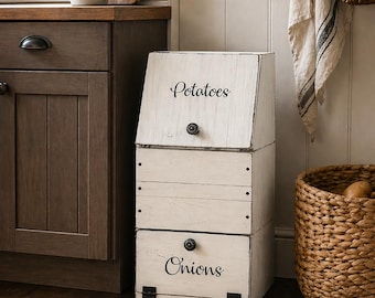 May include: A three-tiered, white wooden storage bin with black hardware. The top bin reads "Potatoes" in script, and the bottom bin reads "Onions". The bin is in a kitchen setting with a woven basket and a plant.