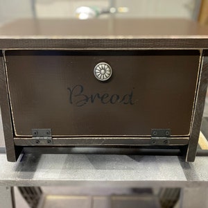 K&ouml;nnte beinhalten: Eine dunkelbraune Brotbox aus Holz mit einem Scharnierdeckel und einem silbernen Knopf. Der Deckel tr&auml;gt eine schwarze Aufschrift mit der Aufschrift "Brot".