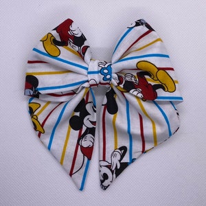 May include: A white bow with red, yellow, and blue stripes featuring a repeated pattern of Mickey Mouse.
