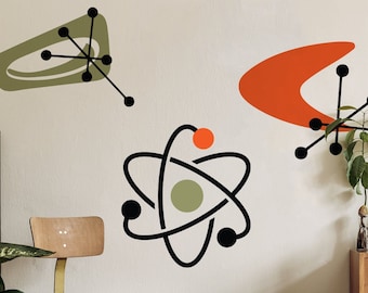 May include: Mid-century modern wall decor featuring abstract atomic shapes in olive green, orange, and black. The room includes a wooden chair, a small stool, a wooden dresser, and a square clock. Plants and decorative items complete the retro aesthetic.