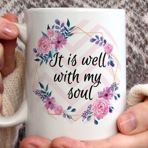 May include: White ceramic mug with a pink and purple floral design and gold geometric accents. The mug features the text "It is well with my soul".