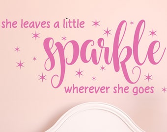 Puede incluir: Pegatina de pared rosa con el texto "she leaves a little sparkle wherever she goes" con estrellas alrededor del texto. La pegatina está en una pared rosa sobre una cuna blanca.