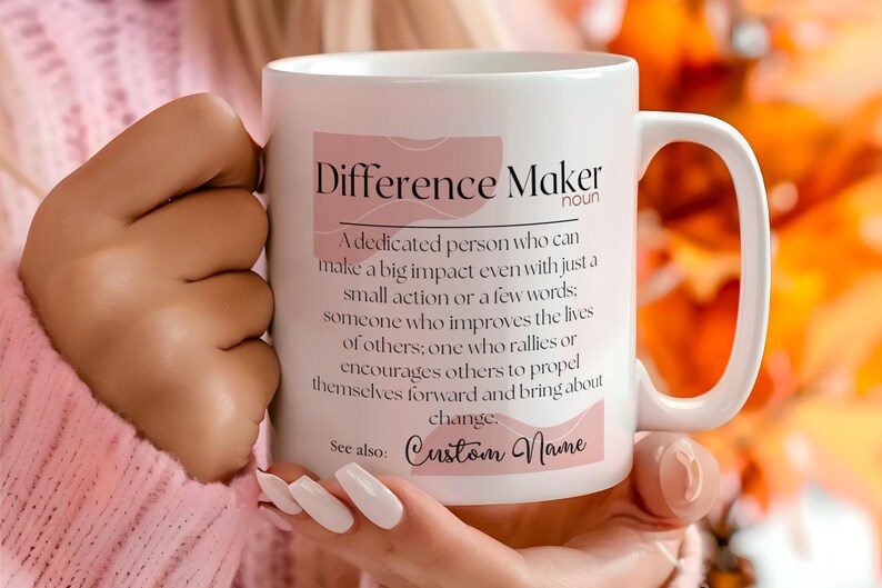 May include: White ceramic mug with a pink and white design. The mug features the text "Difference Maker" and a definition of the word. The text "Custom Name" appears at the bottom of the mug.