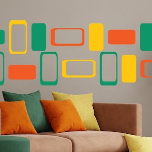 May include: A brown couch with green, orange, and yellow throw pillows in front of a wall with a geometric pattern of green, yellow, and orange rectangles. A potted plant with green leaves is on the right side of the image.