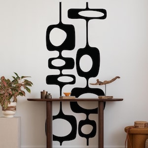 May include: Black and white mid-century modern wall art. The design features abstract shapes with rounded edges. A wooden table with decorative items and a plant in a white pot are in the foreground.