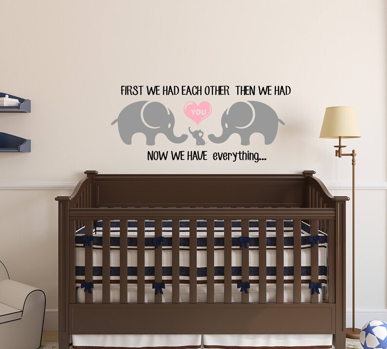 Pu&ograve; includere: Un adesivo da parete per l'asilo nido con due elefanti grigi e un elefante pi&ugrave; piccolo al centro. Gli elefanti tengono un cuore rosa con la parola "you" all'interno. Il testo dice "First we had each other, then we had you. Now we have everything..."