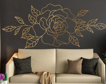 May include: A gold outline of a large flower with leaves on a dark gray wall above a beige couch with two pillows and a throw blanket.