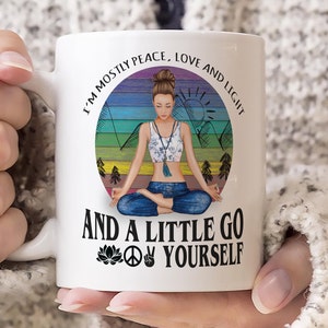May include: White ceramic mug with a colorful illustration of a woman meditating in a circle with the text "I'm mostly peace, love and light and a little go yourself" with a peace sign and a lotus flower.