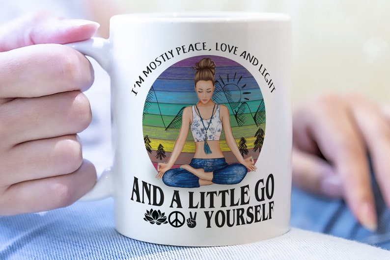 May include: White ceramic mug with a colorful illustration of a woman meditating in front of a mountain range. The text reads "I'm mostly peace, love and light and a little go yourself" with a peace sign and a lotus flower.