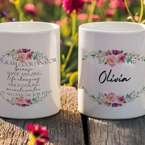 May include: Two white ceramic mugs with floral designs. One mug has the text "PROGRAM COORDINATOR" and other text. The other mug has the name "Olivia". Both mugs have a floral wreath design.