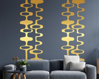 May include: Two gold abstract wall decals in a retro style, featuring a series of connected oval shapes, are applied to a dark blue wall behind a gray sofa.