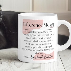May include: White ceramic mug with a pink and white design. The mug has the text "Difference Maker" with a definition and the name "Sophia Winston".