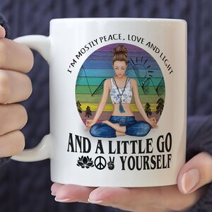 May include: White ceramic mug with a colorful graphic of a woman meditating in a mountain landscape. The text reads "I'm mostly peace, love and light and a little go yourself" with a peace sign, a lotus flower, and a hand gesture.