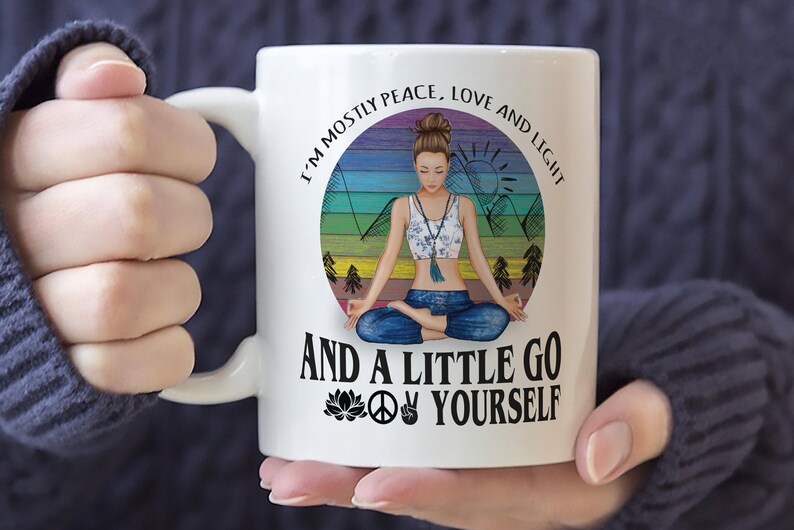 May include: White ceramic mug with a colorful graphic of a woman meditating in a mountain landscape. The text reads "I'm mostly peace, love and light and a little go yourself" with a peace sign, a lotus flower, and a hand gesture.
