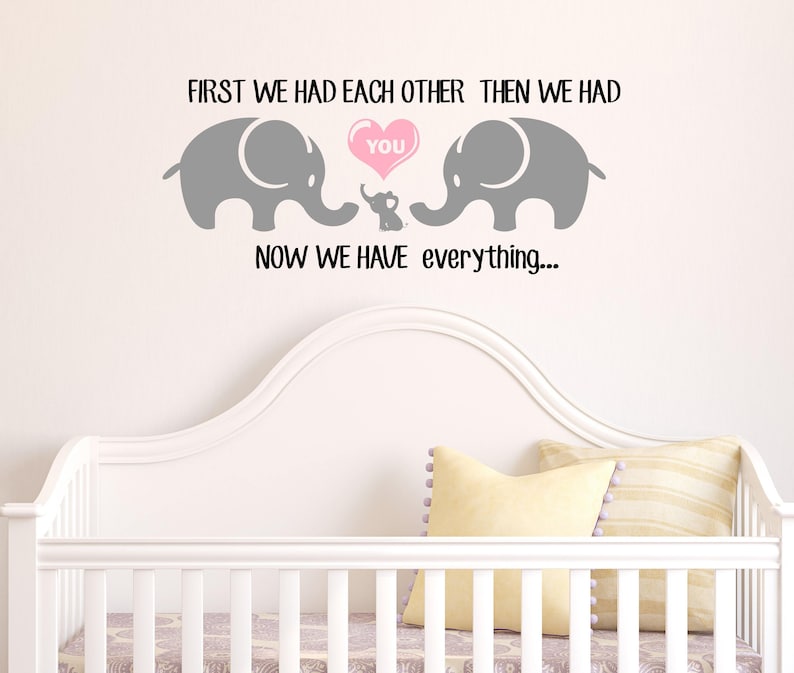 Pu&ograve; includere: Un adesivo da parete per l'asilo con due elefanti grigi e un cuore rosa che dice "You". Gli elefanti si guardano e il cuore &egrave; tra loro. Il testo dice "First we had each other then we had you now we have everything..."