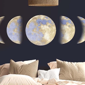 Peut inclure: Un autocollant mural représentant les huit phases de la lune en forme de croissant. Les phases de la lune sont peintes dans un schéma de couleurs bleu clair et or. Les phases de la lune sont disposées en rangée sur un mur bleu foncé.