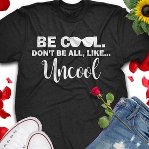 Puede incluir: Camiseta negra con texto blanco que dice "Be Cool. Don't be all, like... Uncool" con un gráfico de gafas de sol.