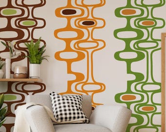 May include: A white wall with three vertical stripes of abstract geometric shapes in brown, orange, and green. The shapes are reminiscent of mid-century modern design. A couch with a white throw and a black and white checkered pillow is in the foreground.