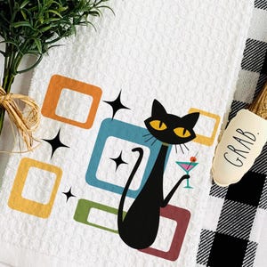 May include: White kitchen towel with a retro design featuring a black cat holding a cocktail, surrounded by colorful geometric shapes and starbursts. A spatula with "GRAB" printed on it is also visible.
