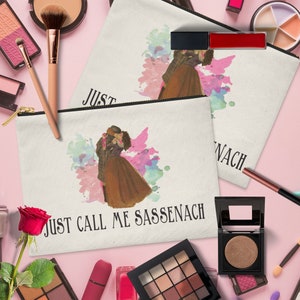 Może przedstawiać: Biała kosmetyczka z płótna z akwarelowym wzorem tańczącej pary. Kosmetyczka ma zamek błyskawiczny i napis "Just Call Me Sassenach" nadrukowany z przodu.