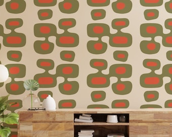 May include: A beige wall with a repeating pattern of green and orange abstract shapes. The wall is behind a wooden console table with a vase and a plant on top.
