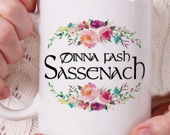 May include: White ceramic mug with a floral design and the text "Dinna Fash Sassenach" in black.