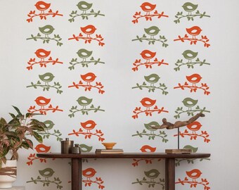 Pode incluir: Uma parede branca decorada com padrões repetidos de pássaros laranja e verdes pousados em galhos. Uma consola de madeira com objetos decorativos está localizada abaixo da arte de parede, e uma planta em vaso está à esquerda.