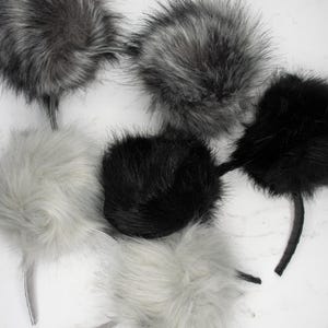 May include: A selection of fluffy, faux fur headbands in shades of grey and black. The headbands feature a round, pom-pom design and a thin, curved band. The fur has a soft, textured appearance.