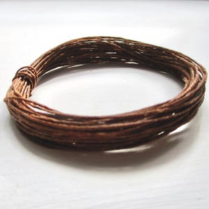 May include: A circular coil of brown twine, tightly wound. The twine appears to be made of natural fibres, with a slightly rough texture. The twine is a warm brown colour, and the coil is resting on a white surface.
