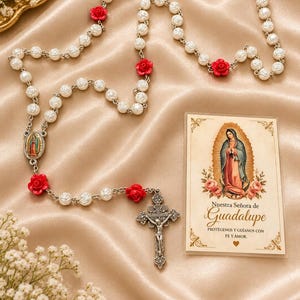May include: A rosary featuring white rose-shaped beads interspersed with red rose beads, a silver-toned crucifix, and a center medal depicting Our Lady of Guadalupe. Beside it is a prayer card with an image of Our Lady of Guadalupe and text.