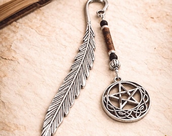 Può includere: Un segnalibro in metallo color argento a forma di piuma, dotato di un ciondolo pendente. Il ciondolo è composto da una perlina cilindrica marrone, due piccole perline sferiche nere e un pendente circolare raffigurante un pentagramma stellato.