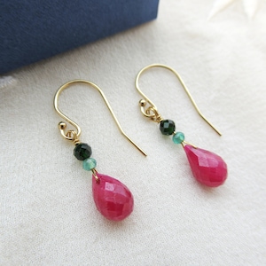 May include: Gold earrings with pink and green gemstone drops. The earrings feature a teardrop-shaped pink gemstone with a smaller green gemstone above it.