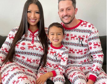 May include: A family wearing matching white and red Christmas pajamas with a reindeer pattern. The pajamas have a red trim and a snowflake design. The family is sitting on a couch.